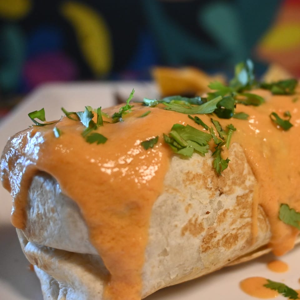 A large burrito from La Reyna Xpress, covered in orange sauce and fresh cilantro.