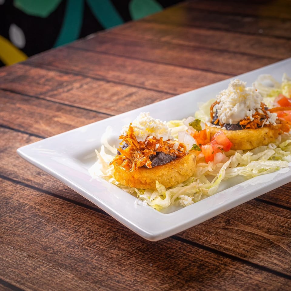 Two La Reyna Xpress sopes with shredded chicken, black beans, cheese, and pico de gallo.