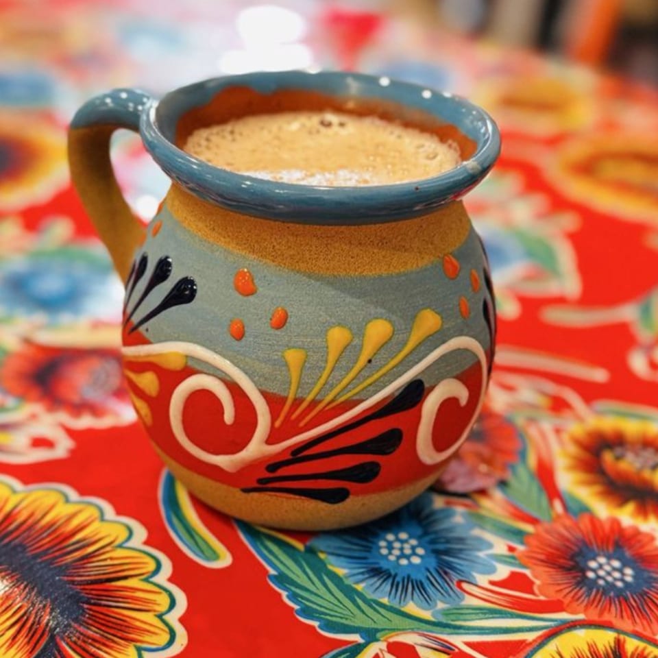 A colorful, hand-painted Mexican mug filled with a frothy beverage sits on a vibrant floral tablecloth.