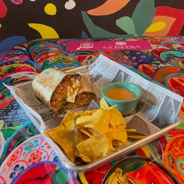 La Reyna Xpress burrito, nachos with cheese, and dipping sauce on a colorful table.