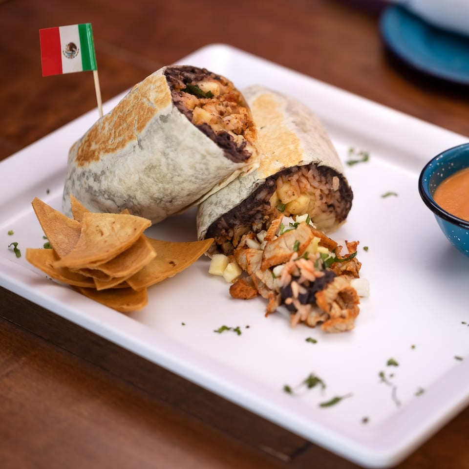 Two La Reyna Xpress burritos with a Mexican flag, tortilla chips, and sauce on a white plate.