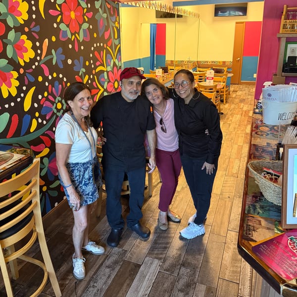 Four smiling people, two men and two women, stand together in a vibrant Mexican restaurant.