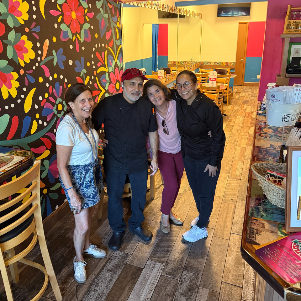 Four smiling people, two men and two women, stand together in a vibrant Mexican restaurant.