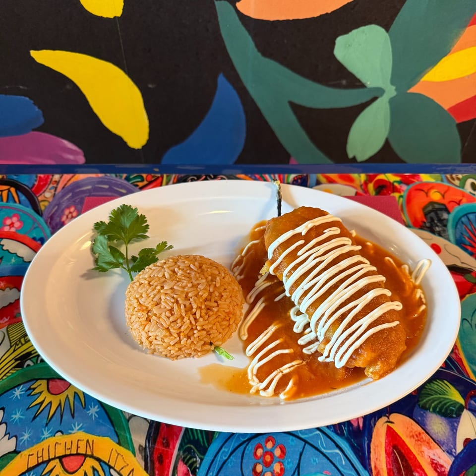 A plate of La Reyna Xpress enchiladas with rice and cilantro, on a colorful patterned table.