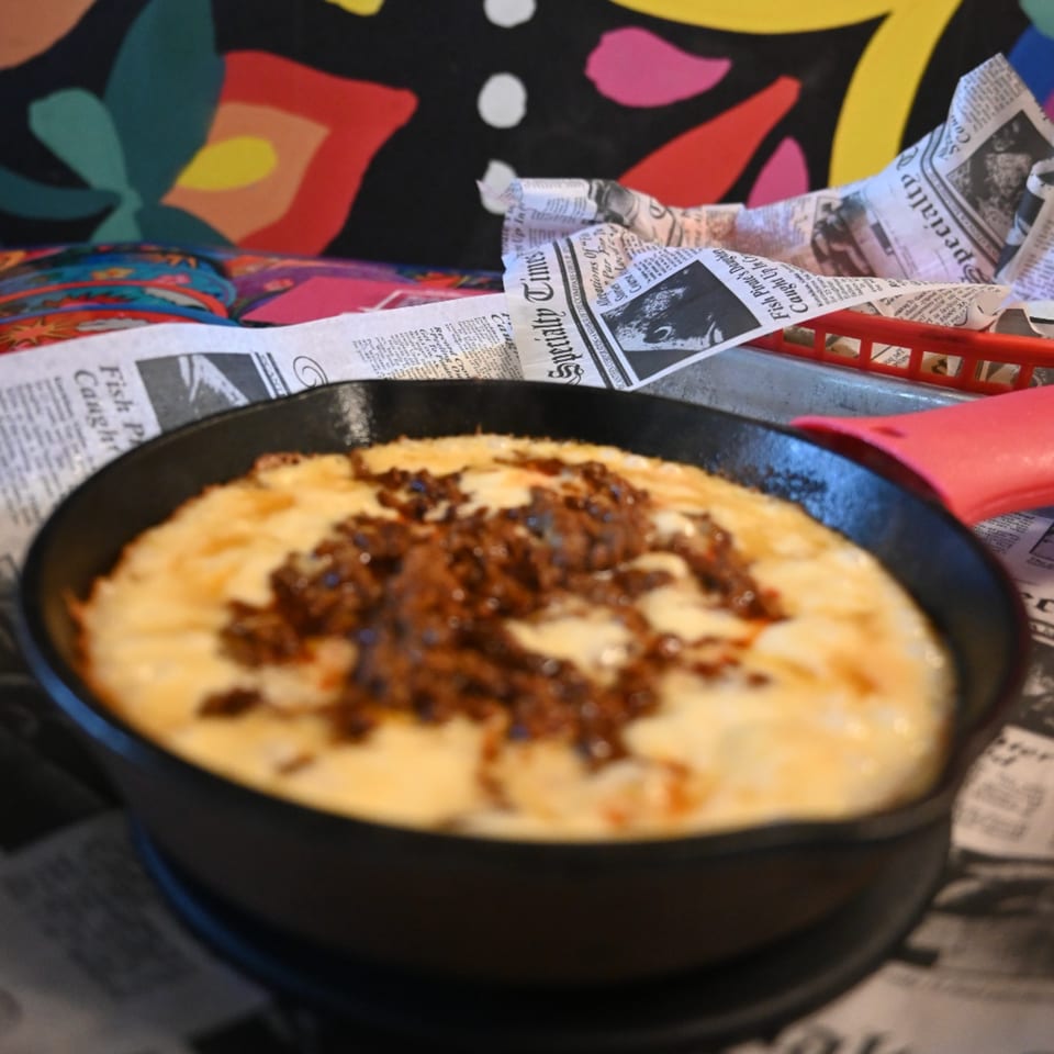 A skillet of melted cheese with chorizo, served on newspaper-lined tray at La Reyna Xpress.
